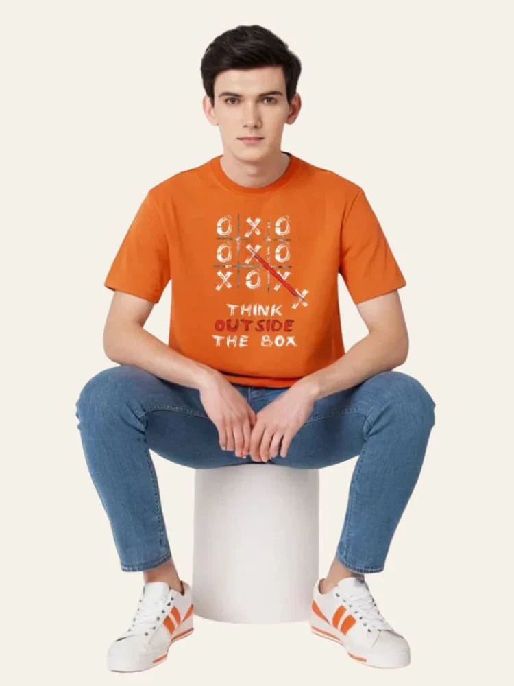 Person wearing an orange t-shirt with a design and text, sitting on a white stool against a light background.