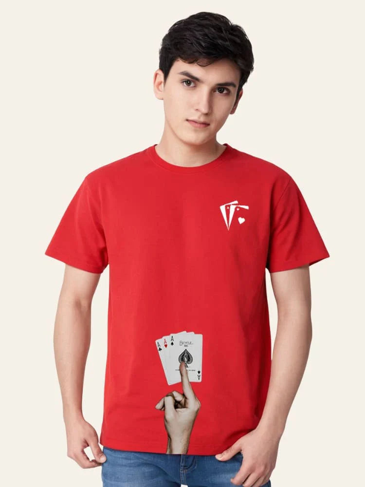 Person wearing a red t-shirt with a logo and playing cards design, holding up a hand with a finger on a beige background.