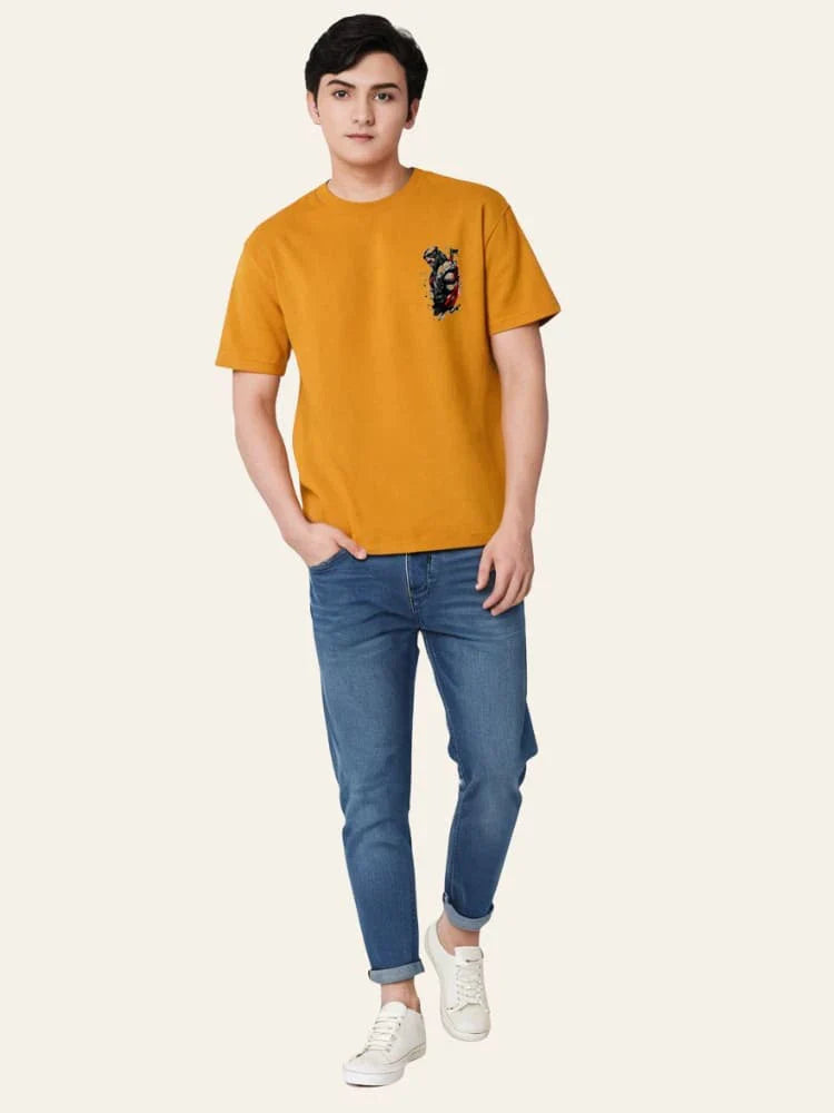 Person wearing a mustard yellow t-shirt with a small graphic and blue jeans on a white background