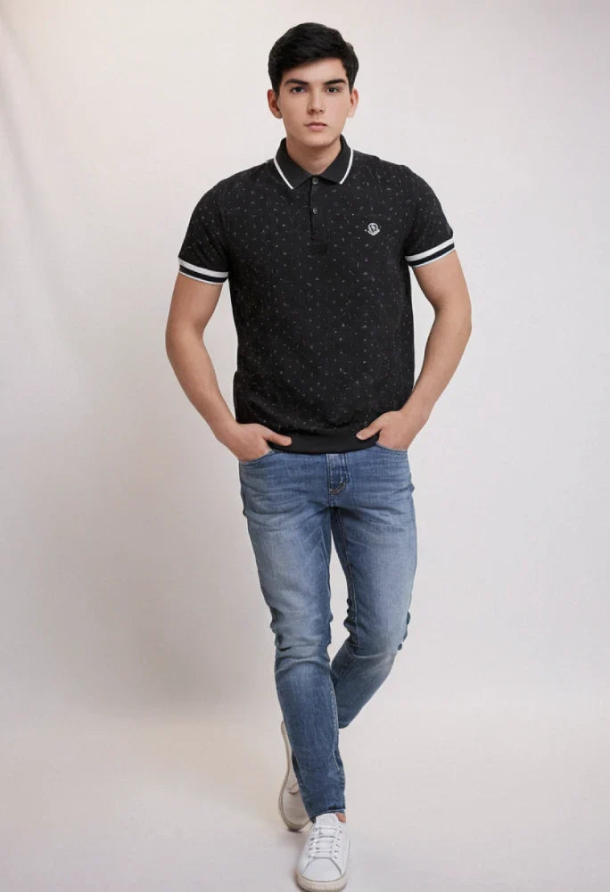 Man wearing a black polo shirt with white trim and blue jeans on a plain background