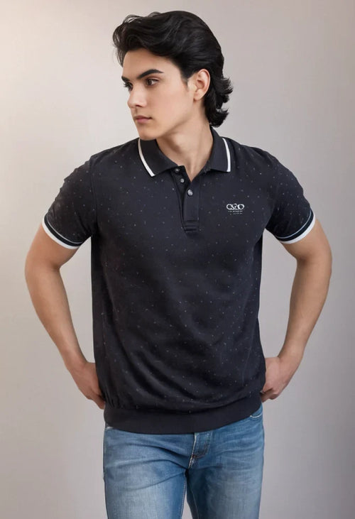 Man wearing a black polo shirt with white trim and a logo, standing against a plain background