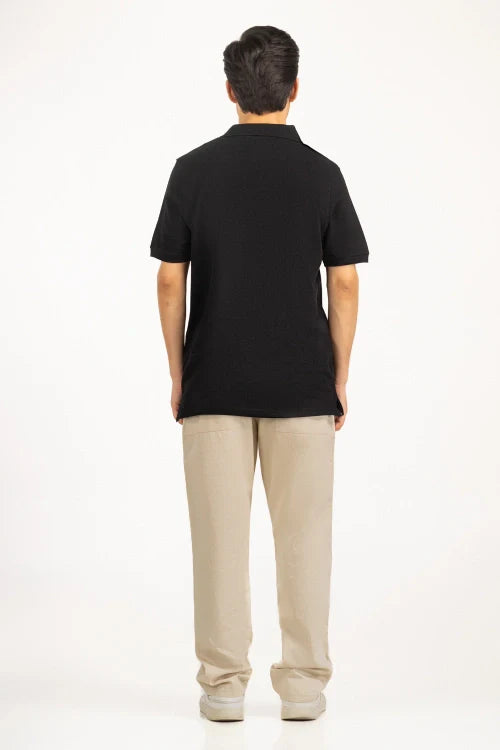 Person wearing a black polo shirt and beige pants on a white background