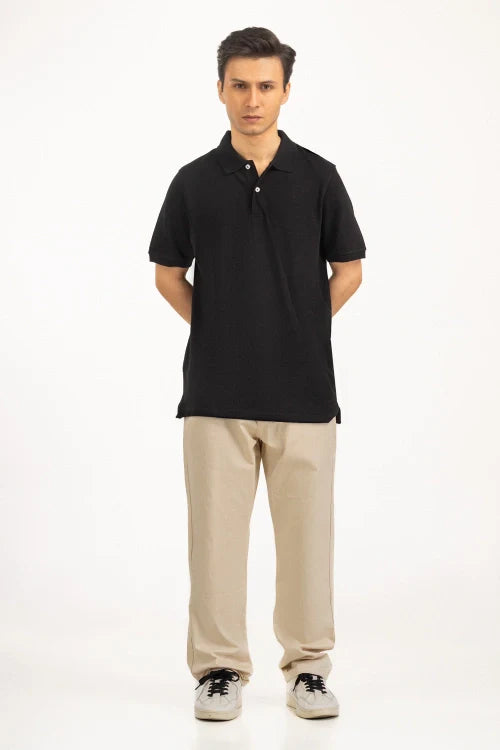 Man wearing a black polo shirt and beige pants on a white background