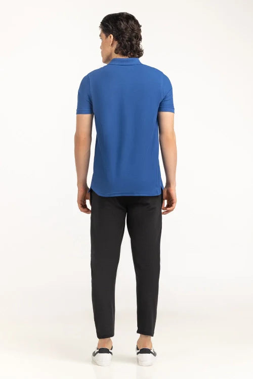 Person wearing a blue polo shirt and black pants on a white background